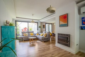A spacious living room with a fireplace, grey sofas, and wooden flooring. - GuestReady - Valdelagrana Gus (El Puerto de Santa María)