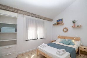 A bedroom with a bed, bedside tables, a wardrobe, a window with curtains, and wall decorations. - GuestReady - Valdelagrana Gus (El Puerto de Santa María)