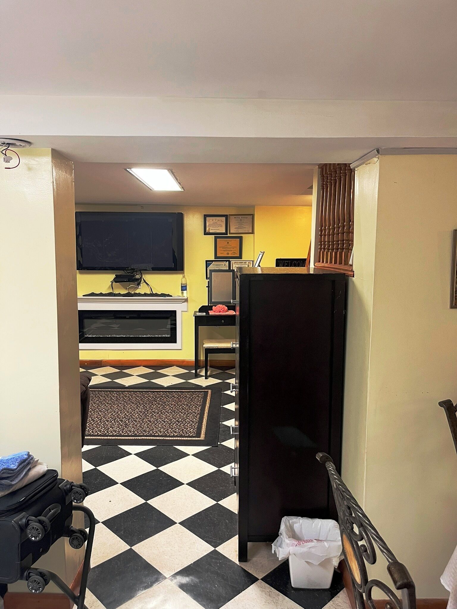 A hotel room with a checkered floor, a bed, a desk with a computer, a television, and a small trash bin.