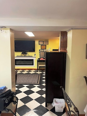 A hotel room with a checkered floor, a bed, a desk with a computer, a television, and a small trash bin.