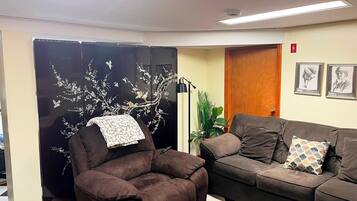 A room with a brown recliner, a black sofa, a decorative black partition with floral designs, a floor lamp, and two framed pictures on the wall.