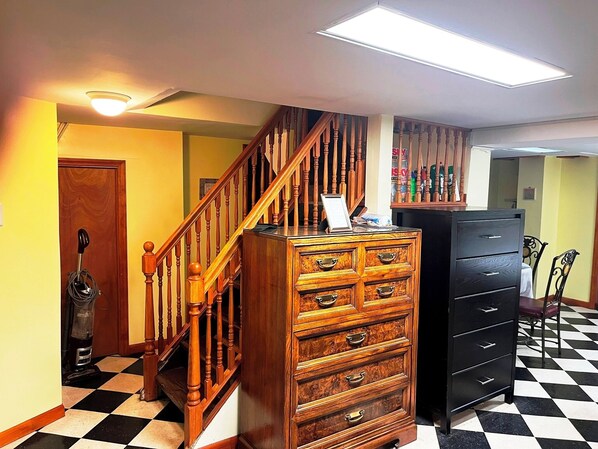 Una escalera con balaustradas de madera, un aparador de madera, un archivador negro y un suelo a cuadros.