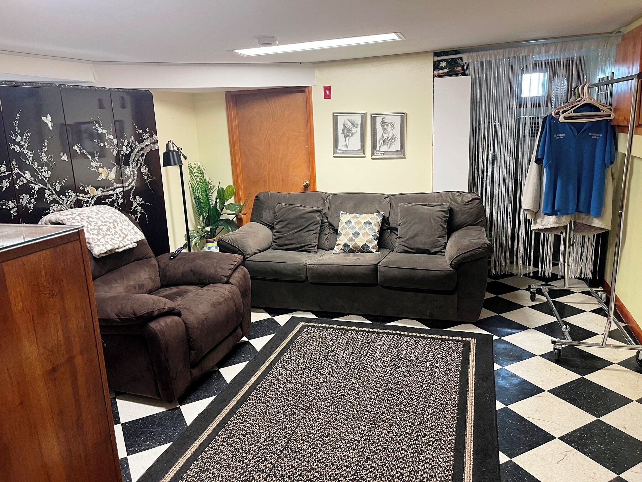 A room with a sofa, a chair, a patterned rug, and a checkered floor.