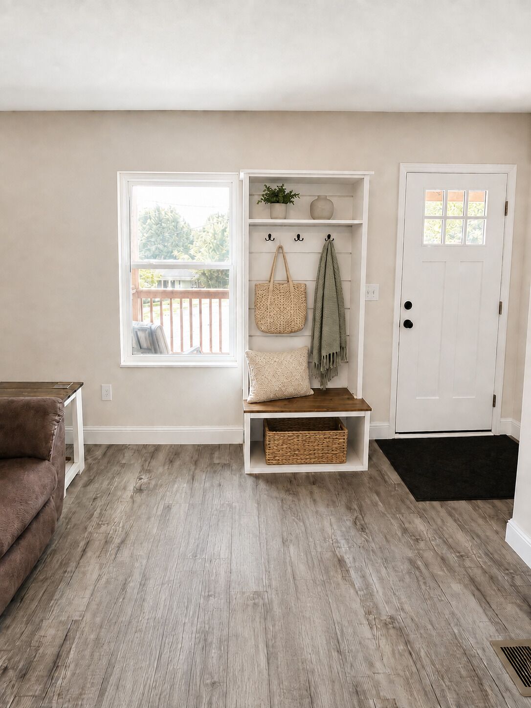 A room with a wooden floor, a bench with a basket, a door, and a window with a view of a deck.