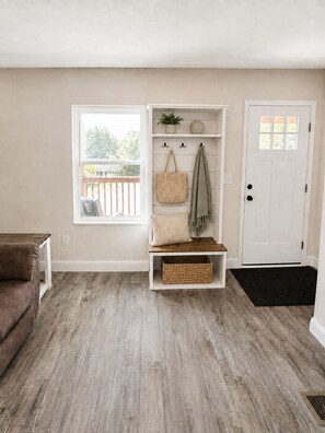 A room with a wooden floor, a bench with a basket, a door, and a window with a view of a deck.