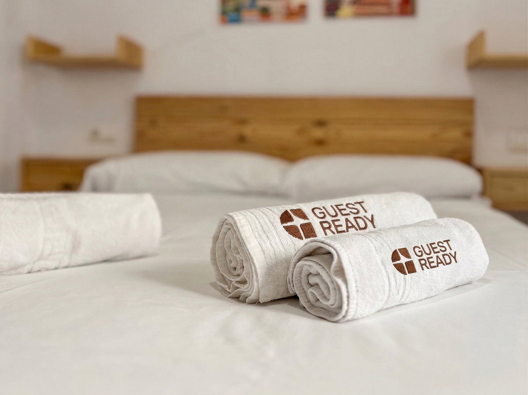 A neatly made bed with white linens and two rolled towels with 'GUEST READY' text.