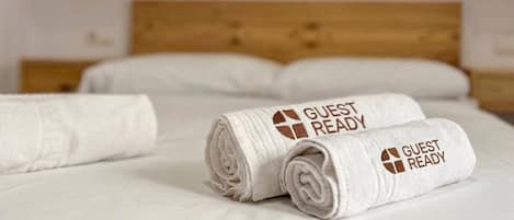 A neatly made bed with white linens and two rolled towels with 'GUEST READY' text.