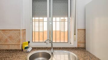 Una cocina con un lavamanos de acero inoxidable, una ventana con persianas y un salpicadero de azulejos.