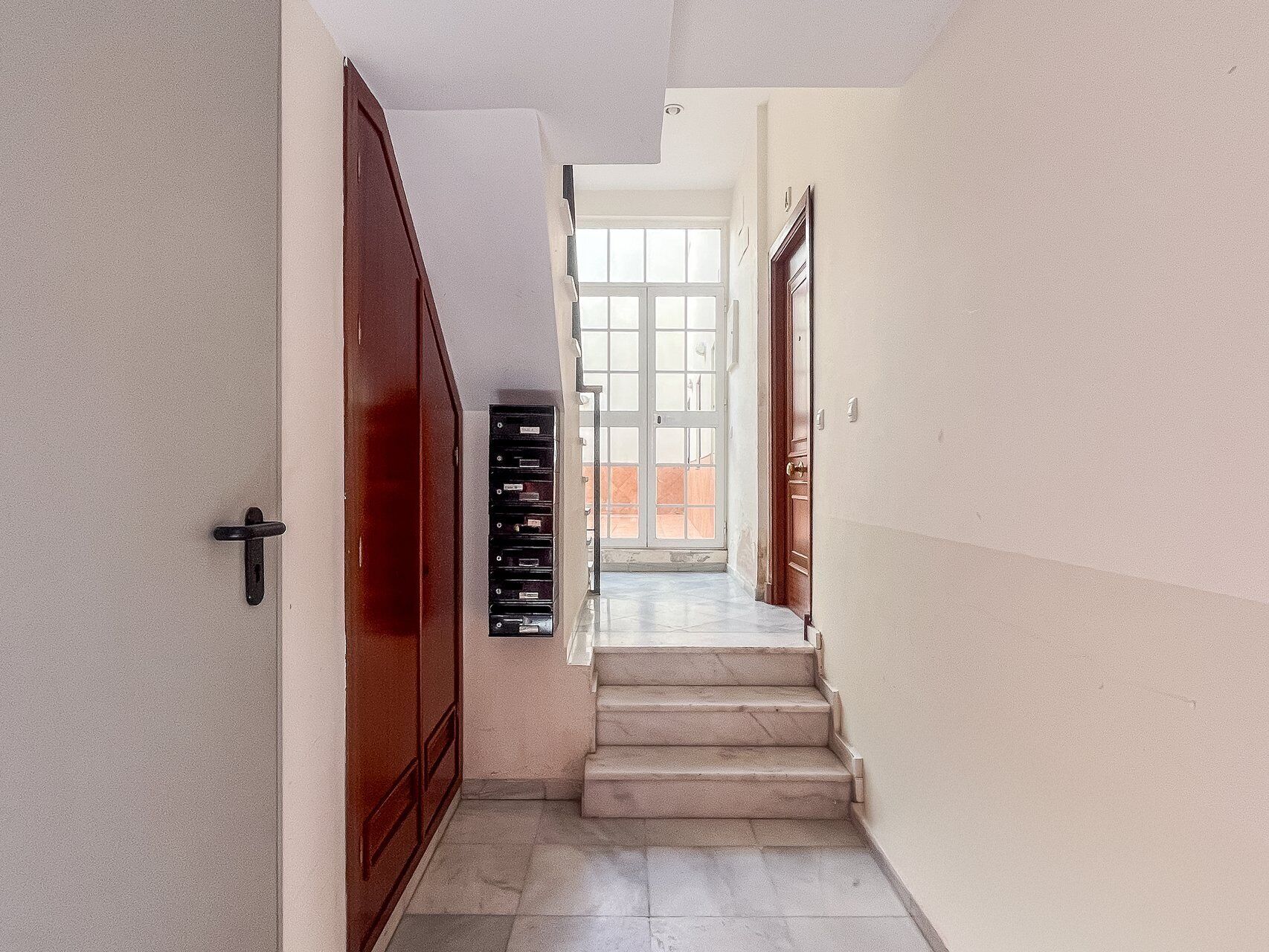 Un pasillo con una escalera que lleva a una puerta con un panel de vidrio.
