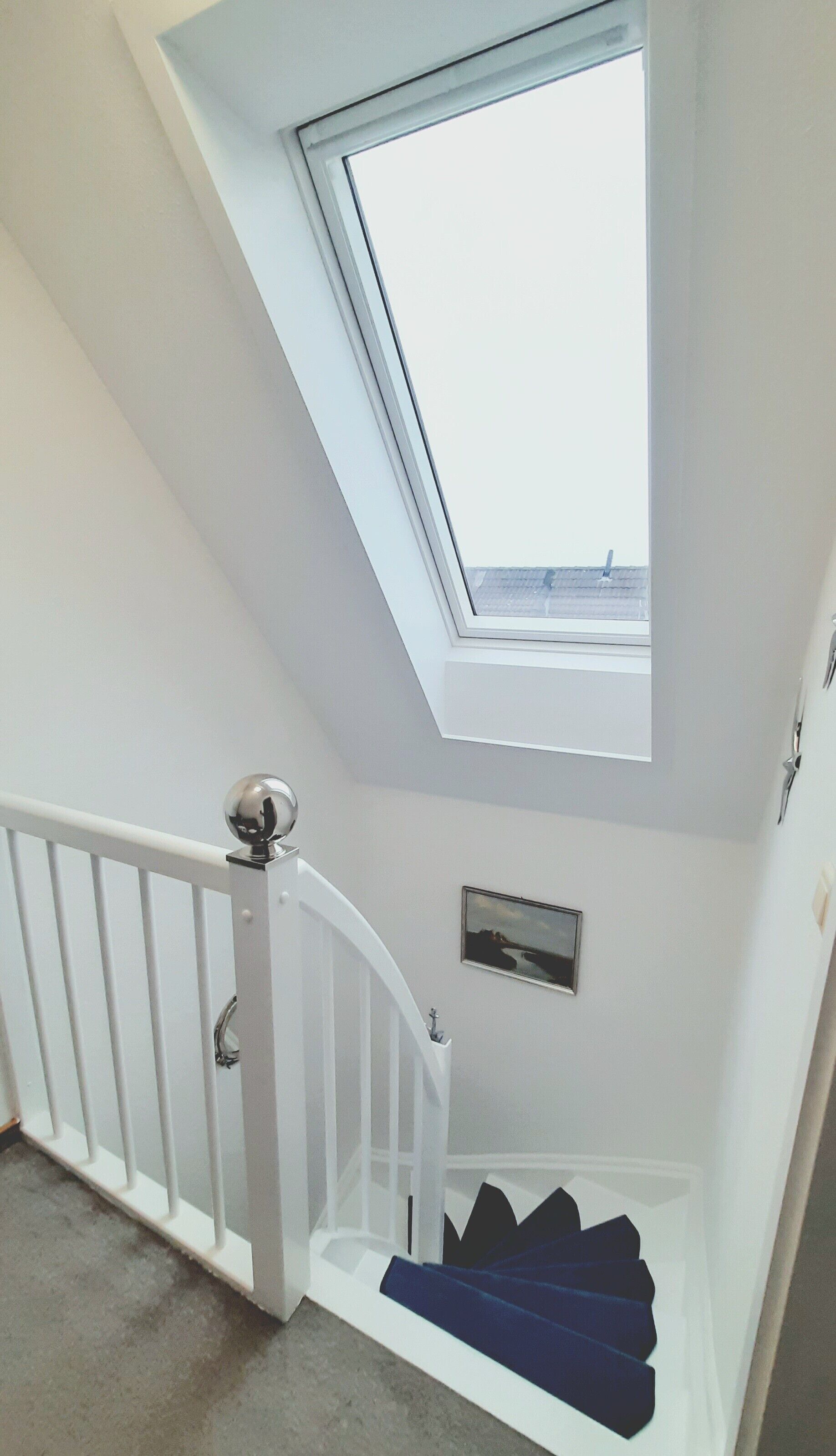 A staircase with a white railing leading to a landing with a skylight.