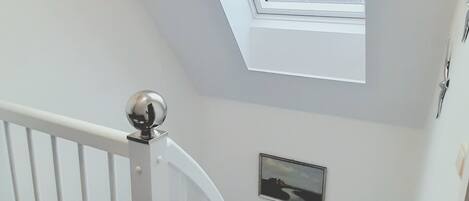A staircase with a white railing leading to a landing with a skylight.