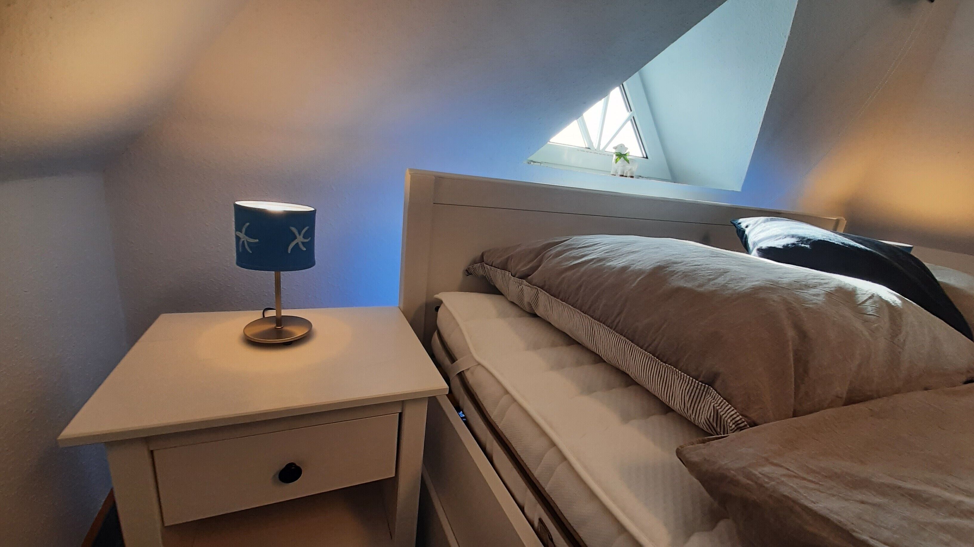 Ein Schlafzimmer mit einem Bett, einem Nachttisch mit Lampe und einem Oberlicht.