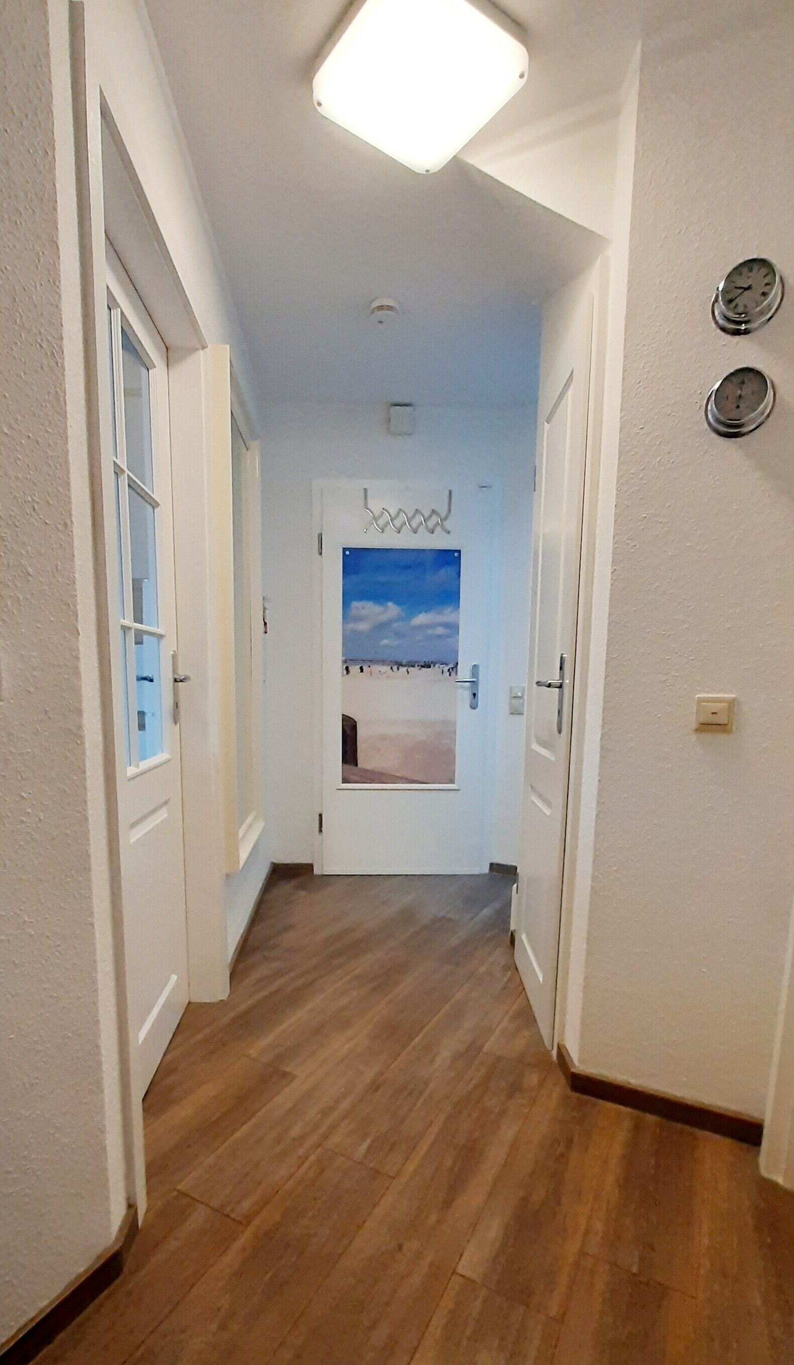Ein Flur mit Holzboden, weißen Wänden und einer Tür mit einer Strandansicht.