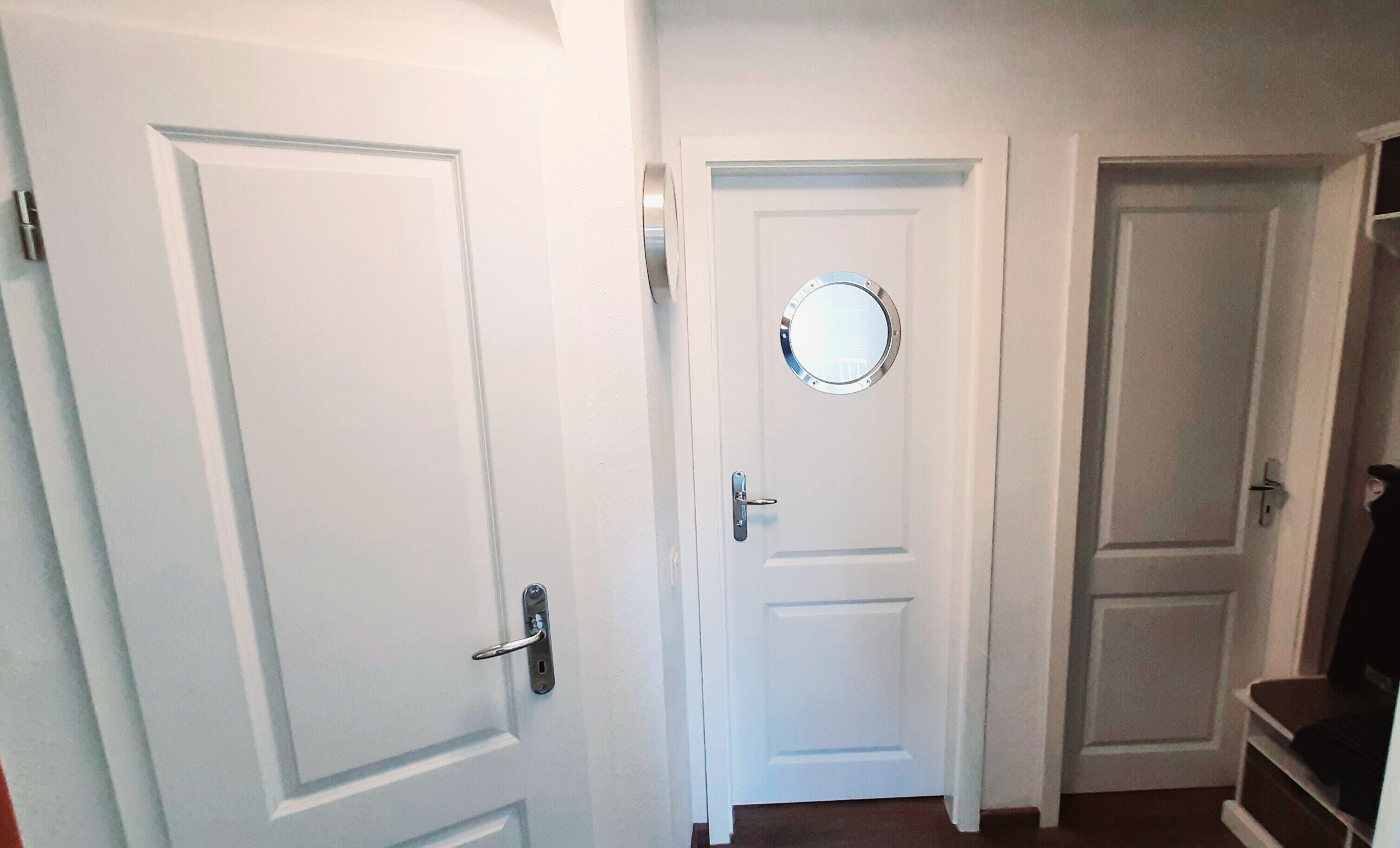 A hallway with three white doors, one with a round mirror above it.