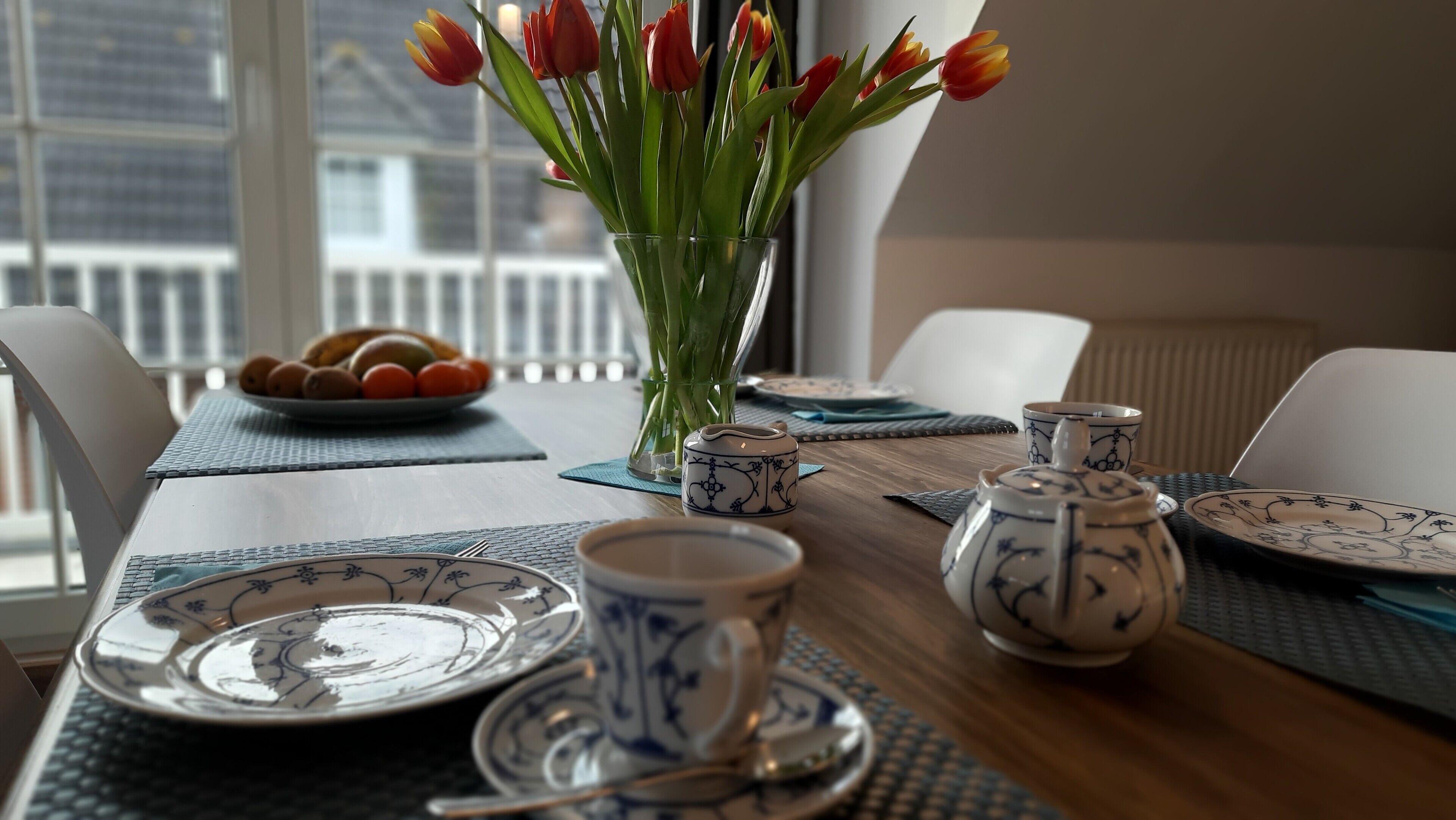 A dining table with a vase of tulips, a fruit bowl, and tea set.