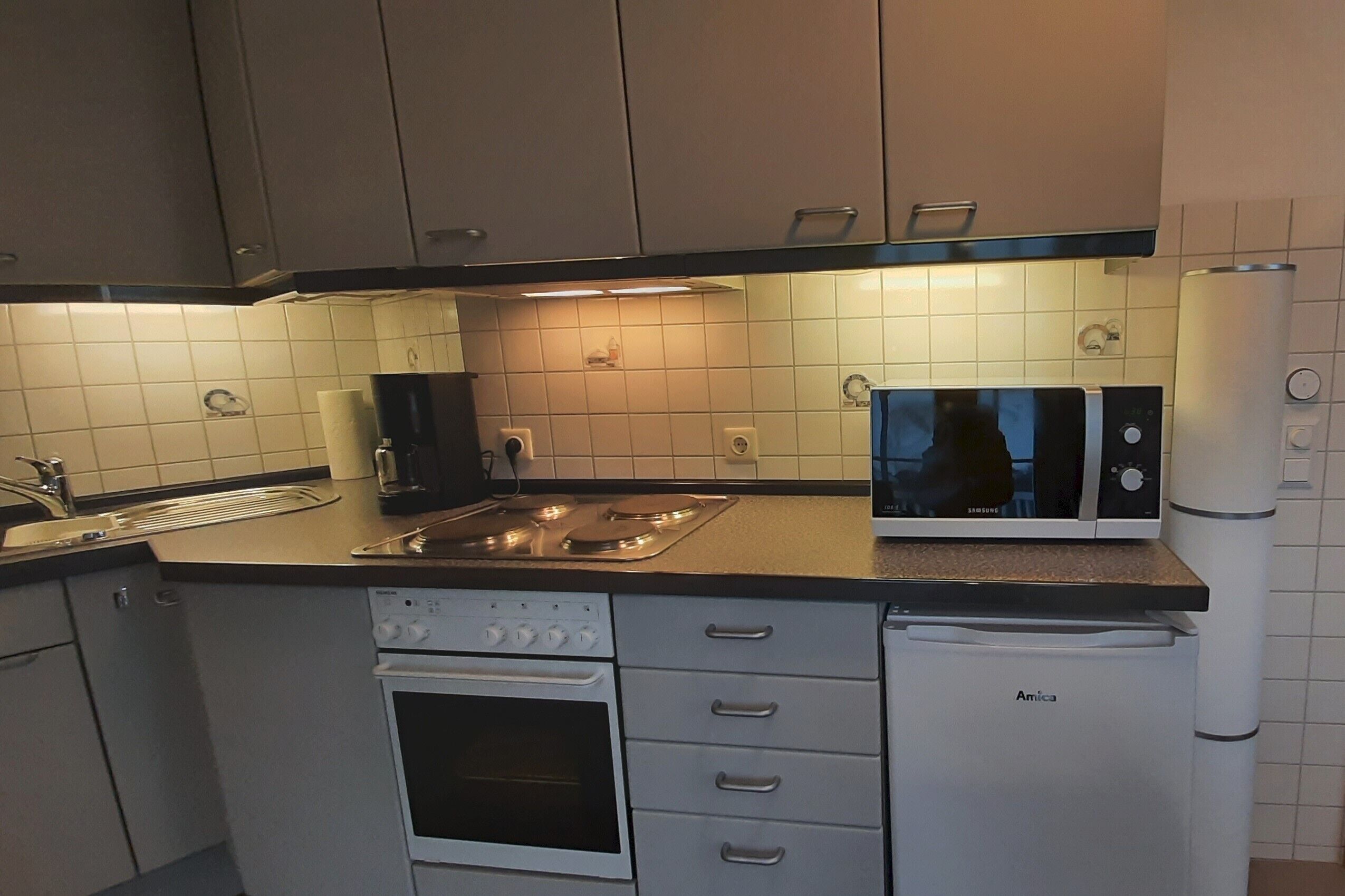 Uma cozinha compacta com forno embutido, micro-ondas e frigorífico.