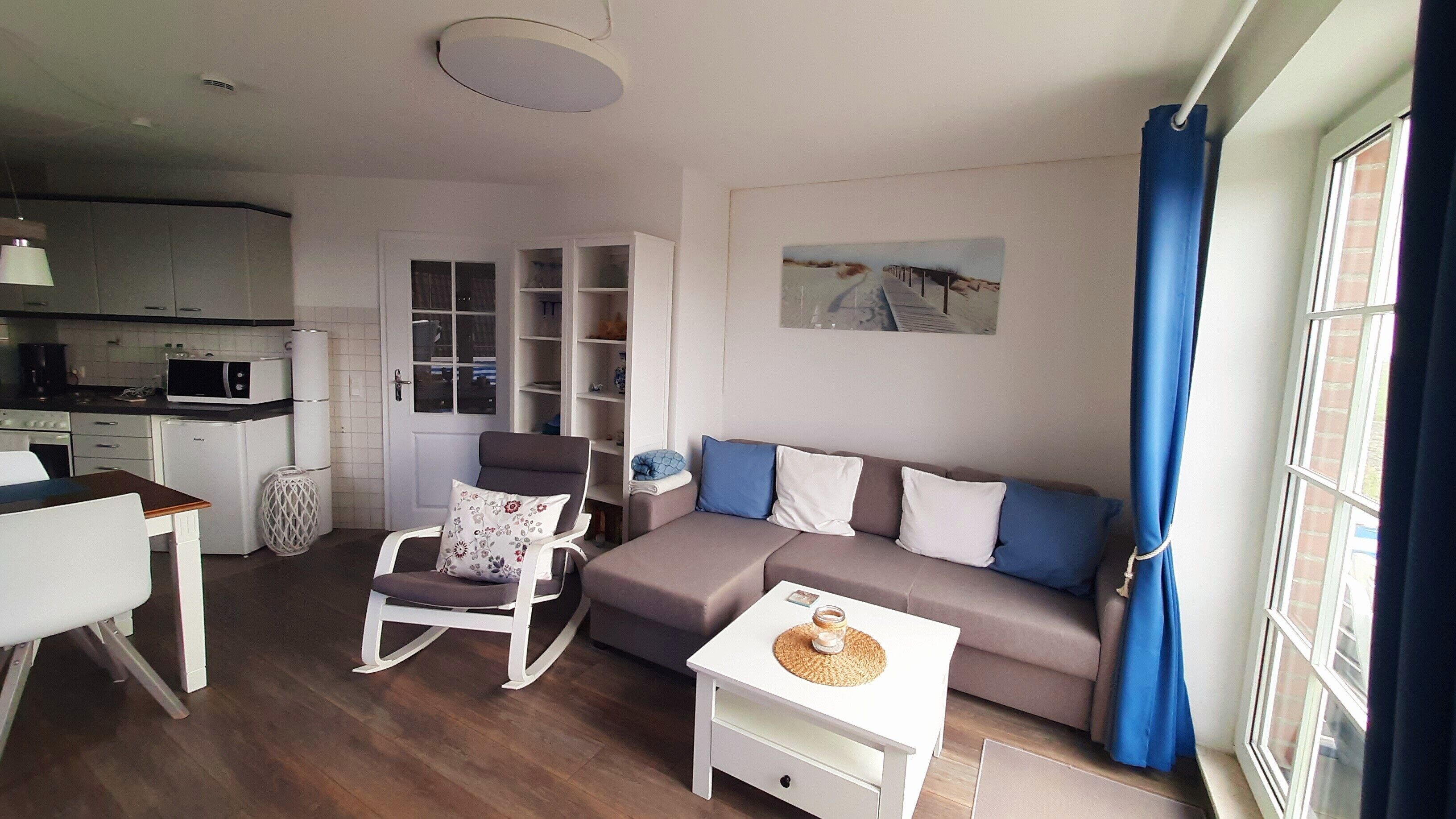 A compact living space with a kitchenette, a sofa set, a dining table, and a chair.