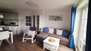 A compact living space with a kitchenette, a sofa set, a dining table, and a chair.