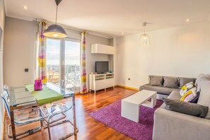 Ein modernes Wohnzimmer mit einem Glastisch, einem grauen Sofa und einem Fernseher im Hintergrund.