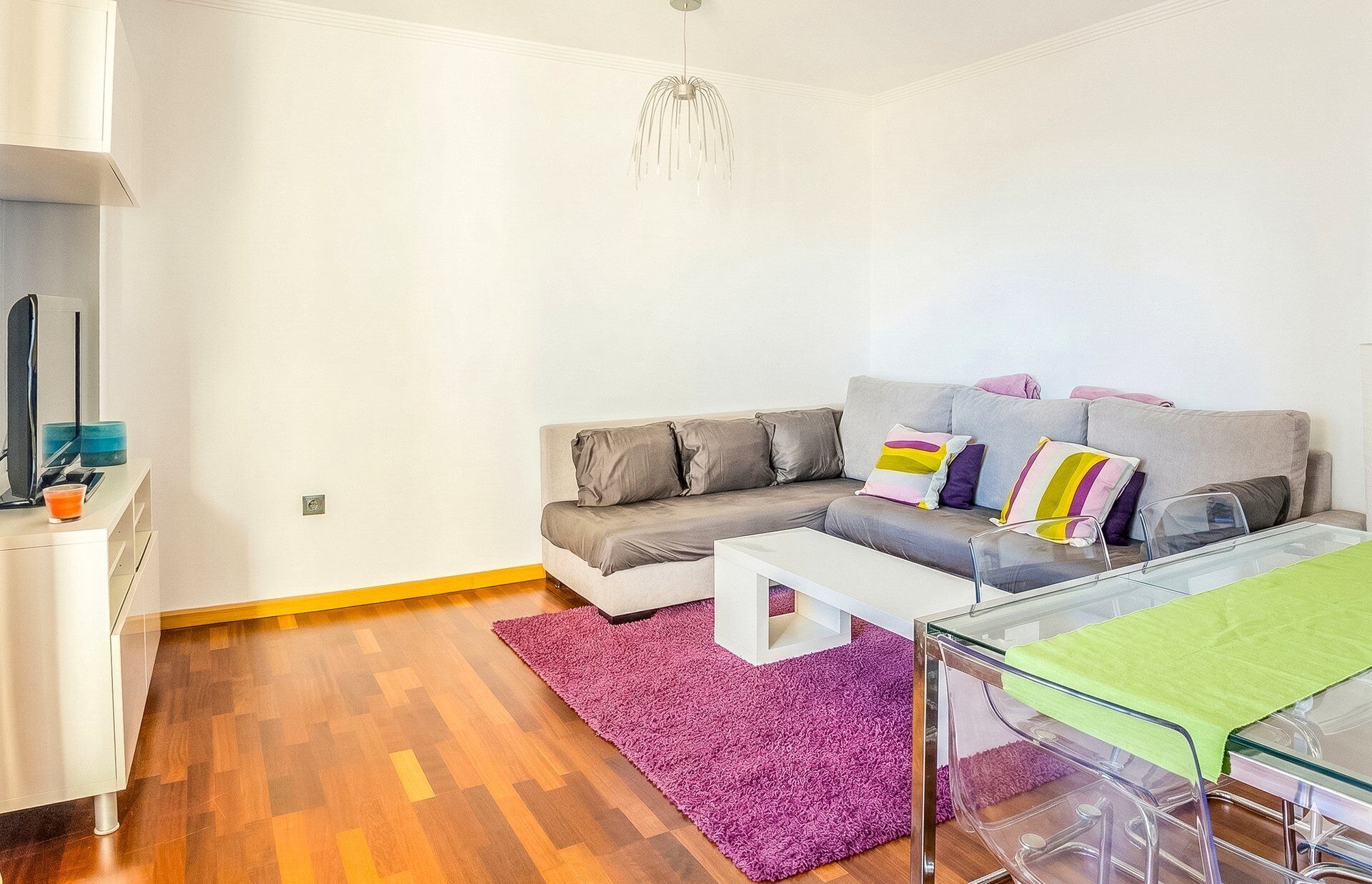A modern living room with a grey sofa, a white coffee table, and a purple rug.