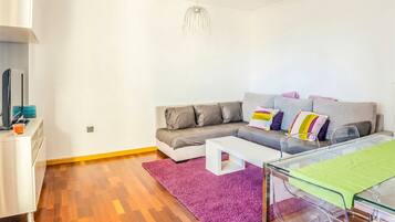A modern living room with a grey sofa, a white coffee table, and a purple rug.