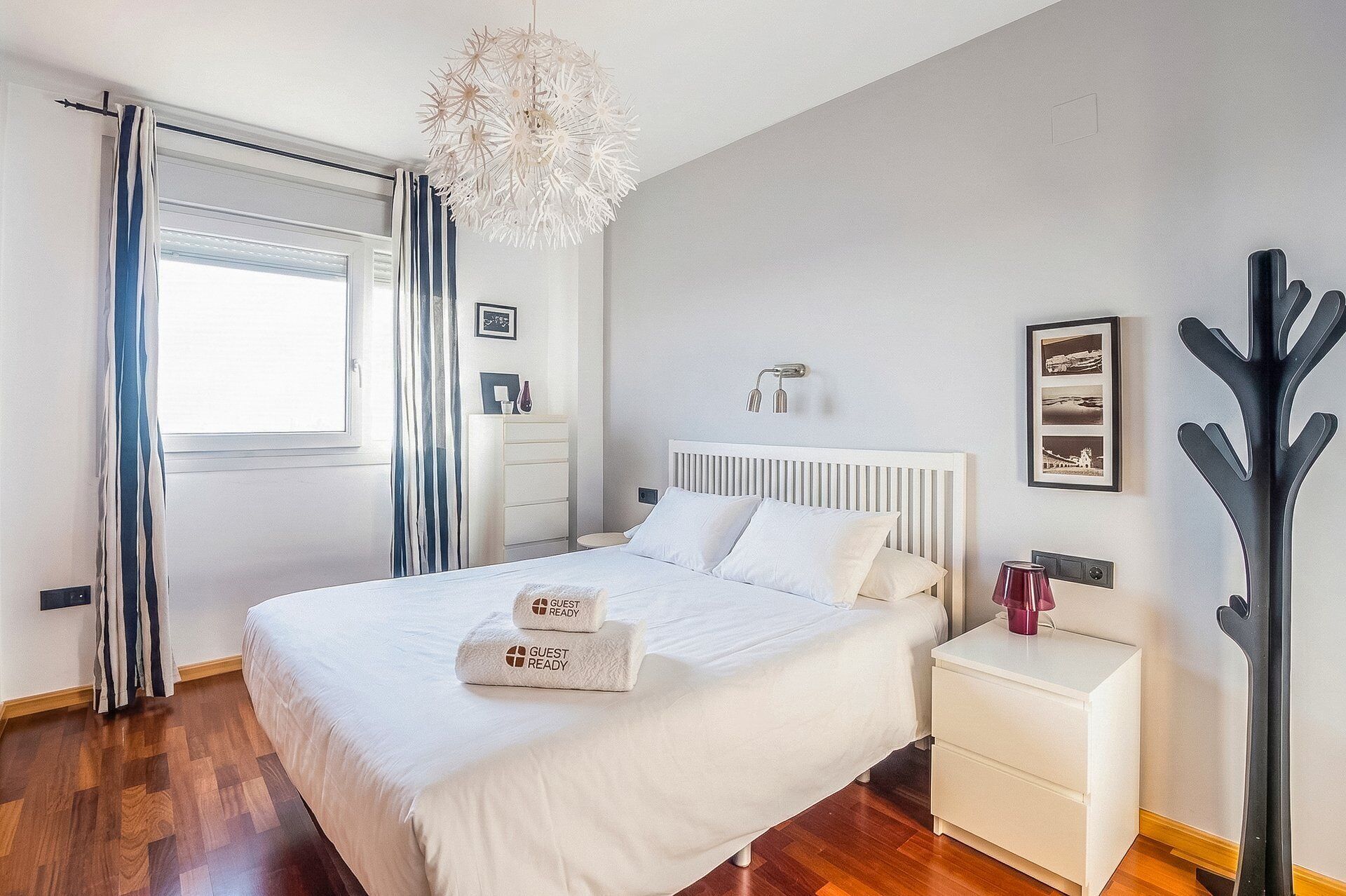 A hotel room with a bed, bedside table, nightstand, and a modern chandelier.