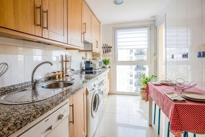 A modern kitchen with a granite countertop, stainless steel sink, and wooden cabinets. - GuestReady - San Fernando Torres de la Caseria JP (San Fernando)