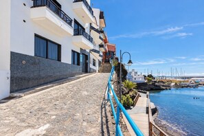 Un bâtiment situé sur la côte, doté d’un escalier en pierre menant à une terrasse en bois qui offre une vue sur un port de plaisance.
