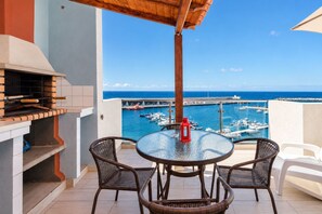 A balcony with a grill, wicker chairs, a glass table, and a view of the sea and boats. - GuestReady - Beachfront Apartment Panoramic Views (La Restinga)