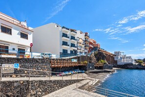 A coastal building with multiple balconies, a stone wall, and a clear blue sky. - GuestReady - Beachfront Apartment Panoramic Views (La Restinga)