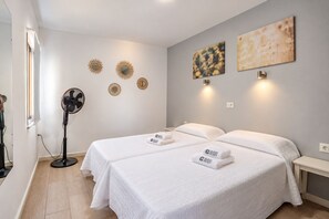 A hotel room with two beds, a standing fan, and wall-mounted artwork. - GuestReady - Beachfront Apartment Panoramic Views (La Restinga)