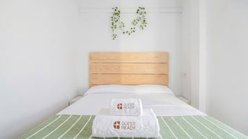 Ein Einzelbett mit Holz Kopfteil, zwei weiße Handtücher mit dem Aufdruck 'GUEST READY' und eine grün gestreifte Bettdecke.