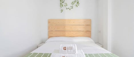 A single bed with a wooden headboard, two white towels with 'GUEST READY' text, and a green-striped bedspread.