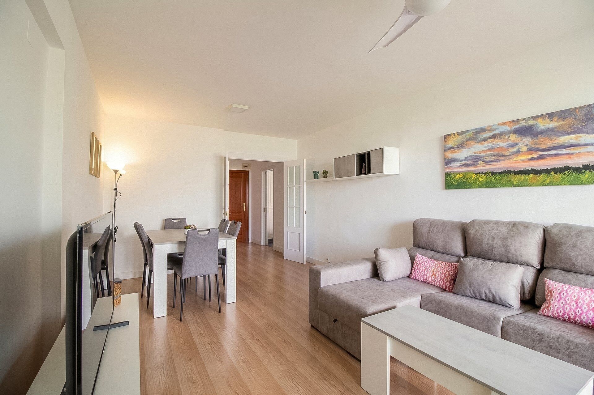 Ein modernes Wohnzimmer mit einem grauen Sofa, einem Esstisch mit Stühlen und einem Bild an der Wand.