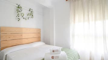 Una cama bien hecha con cabecera de madera, manta a rayas verde y blanca, y dos toallas blancas con el texto 'GUEST READY'.