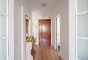 A hallway with a wooden door, a mirror, a vase with flowers, and a small table with a lamp. - GuestReady - Valdelagrana Nacita (El Puerto de Santa María)