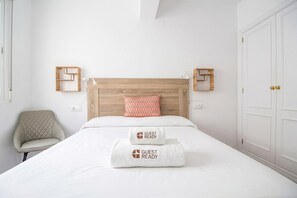 Ein Hotelzimmer mit einem hölzernen Kopfteil, einem Einzelbett mit weißer Bettwäsche, einem roten Kissen mit Muster, zwei Wandleuchten, einem Sessel und einem Kleiderschrank.