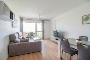 Een moderne woonkamer met een bank, eettafel, stoelen, een televisie en een plafondventilator.