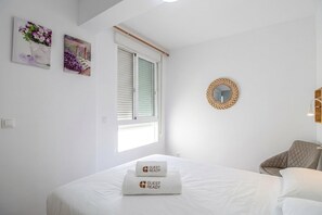 Een hotelkamer met een bed, een raam met zonwering, een wandspiegel en twee ingelijste foto's.