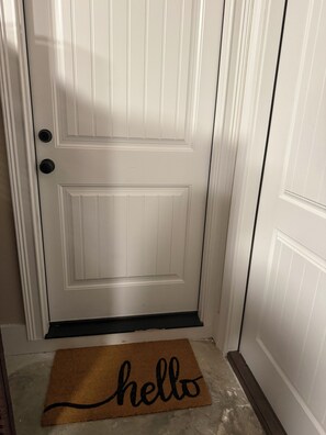 A white door with a doormat that reads 'hello' and a black doorknob.