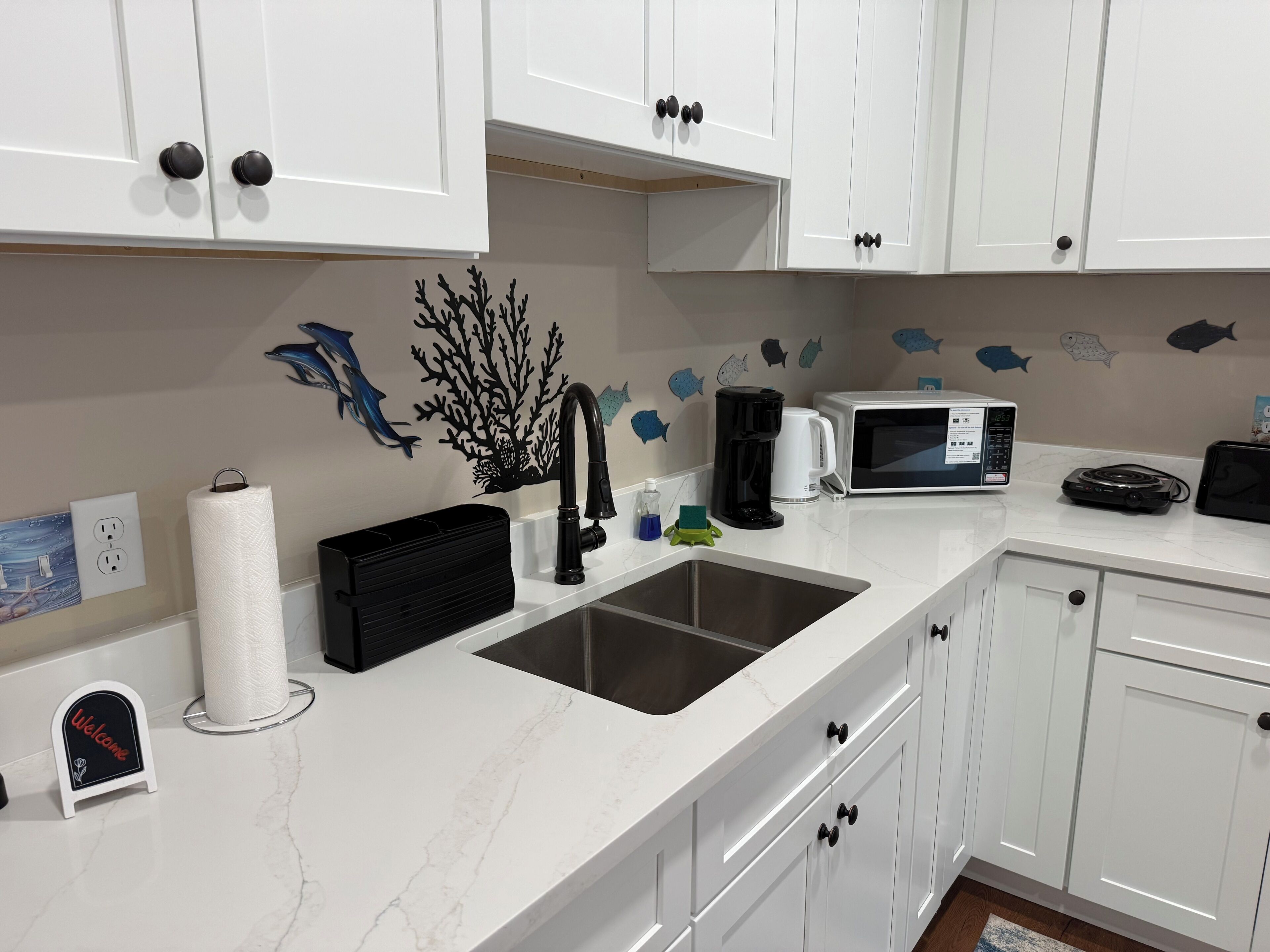 A modern kitchen with white cabinets, a black faucet, a microwave, a coffee maker, and a roll of paper towels.