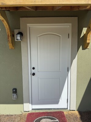 A white door with a keyhole and a doorbell, a mailbox, and a red doormat with a circular design. - New listing Cozy 1 BR 1 BA Apt near beaches priv entrance experienced hosts. (Brunswick)