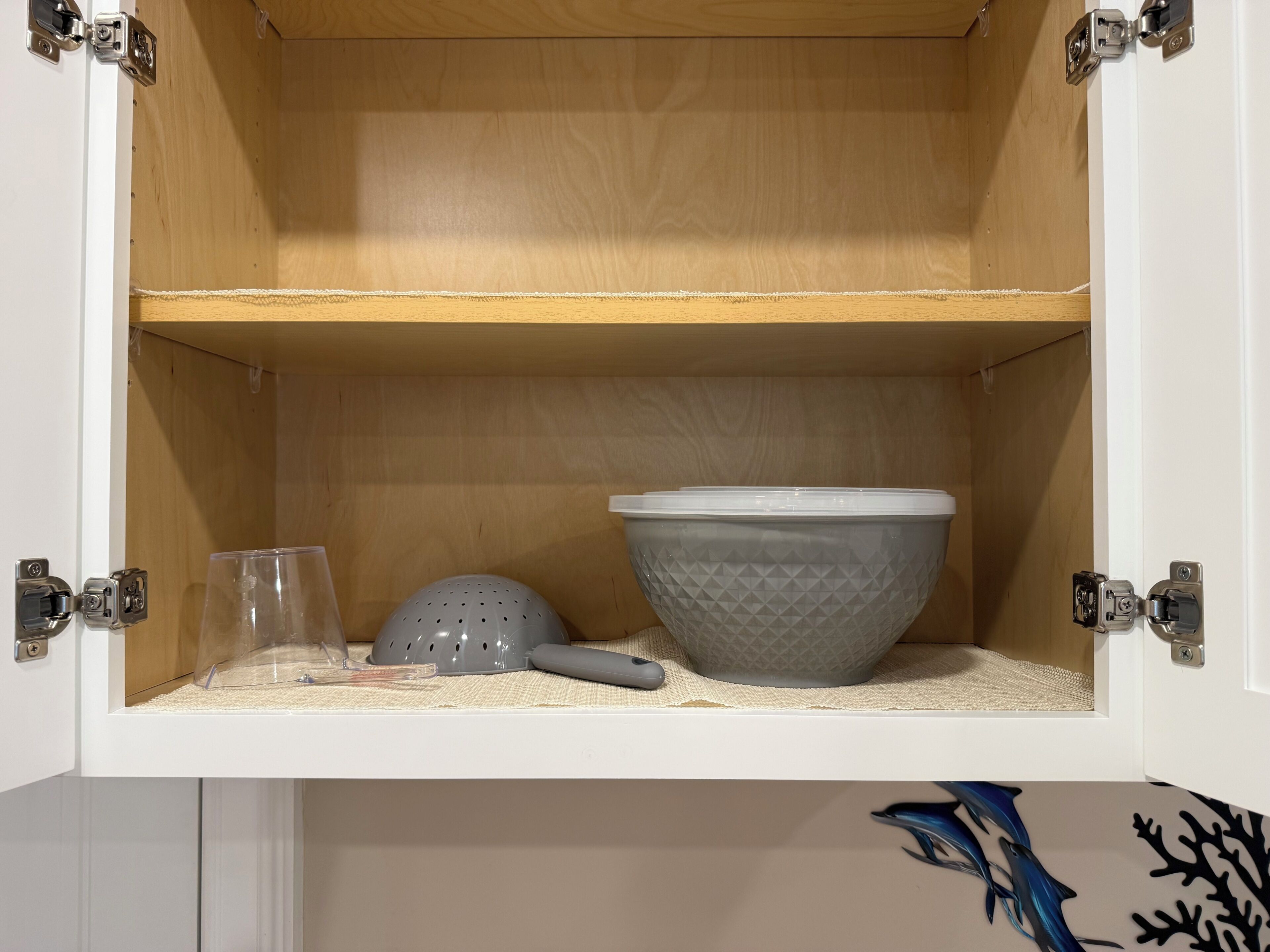 Un pensile da cucina con interno in legno, un bicchiere trasparente, un colapasta grigio e una ciotola grigia dalla superficie ruvida.