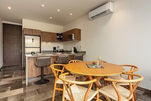 Una cocina moderna con refrigerador empotrado, cafetera y microondas. Hay una zona de comedor con una mesa de madera redonda y sillas de mimbre.