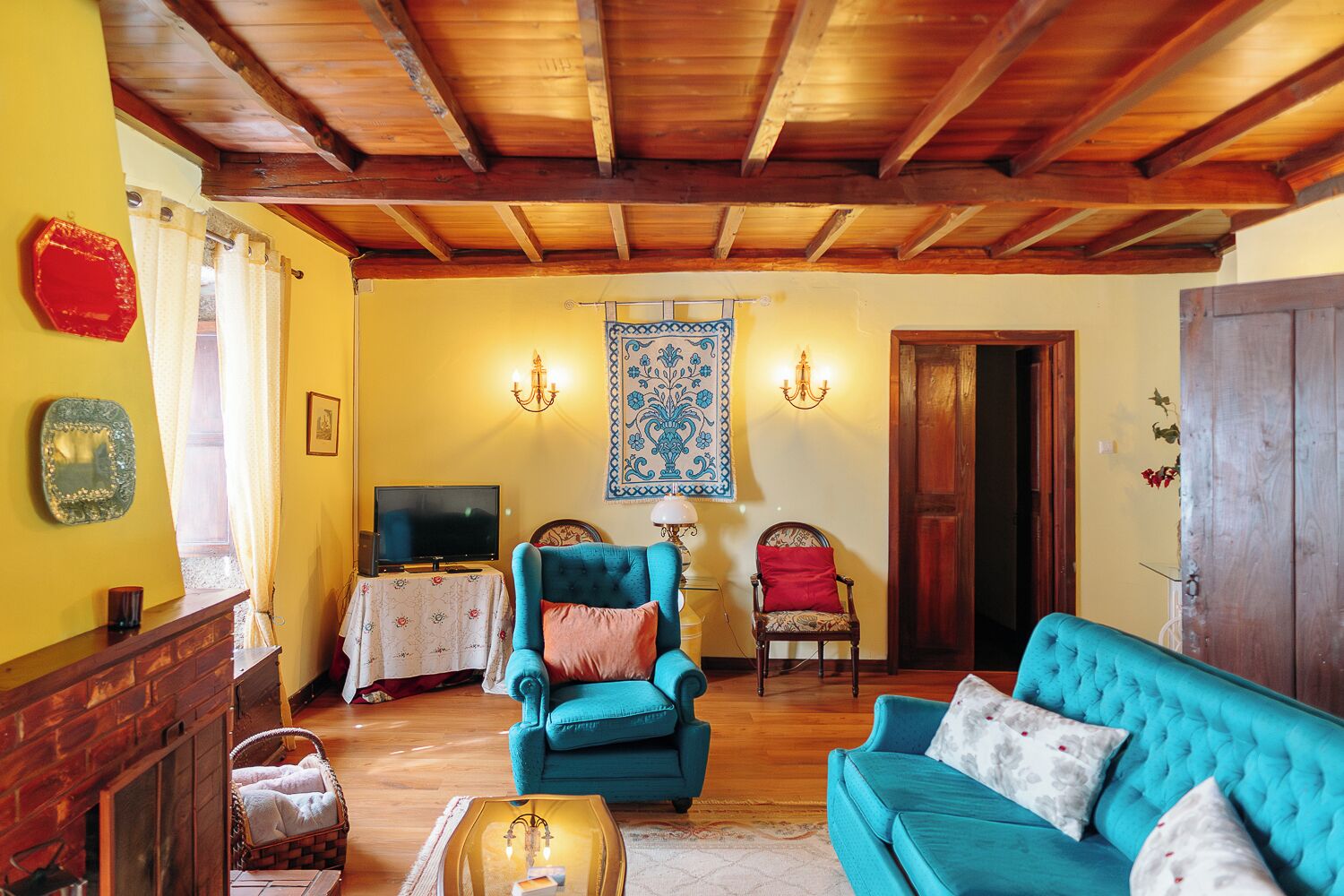 Een gezellige woonkamer met een houten plafond, een televisie, een blauwe bank en een wanddecoratie met een patroon.