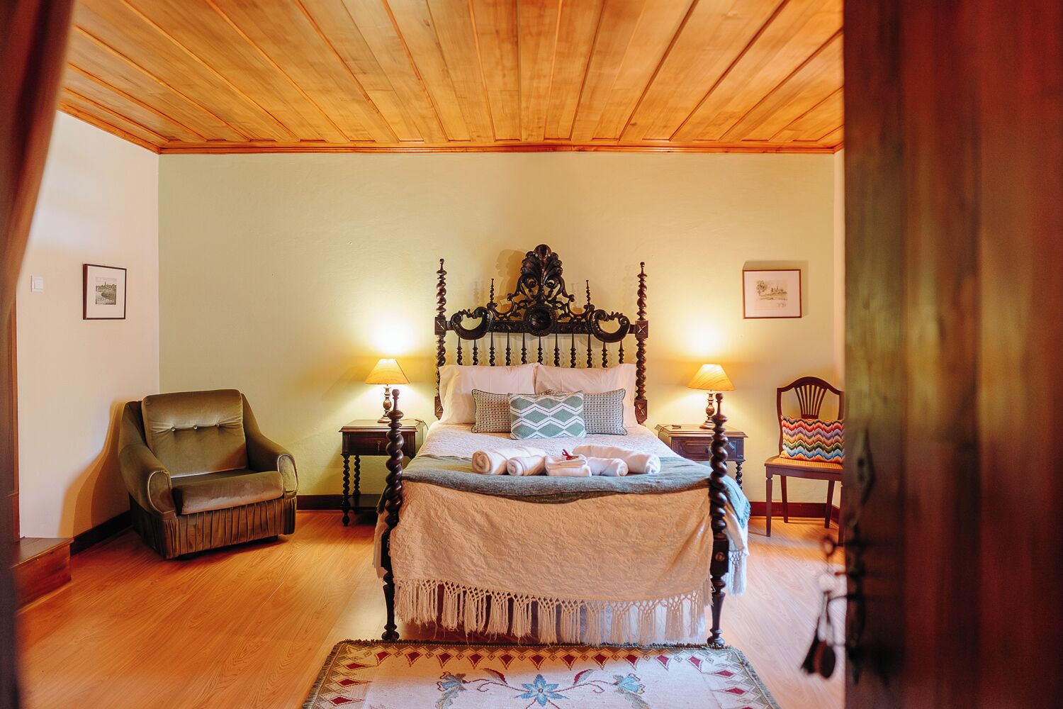 Ein Schlafzimmer mit Himmelbett, Holzboden, Stuhl, Teppich und zwei Nachttischlampen.