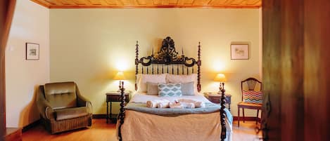 Un dormitorio con cama con dosel, techo de madera, una silla, un tapete y dos lámparas de noche.