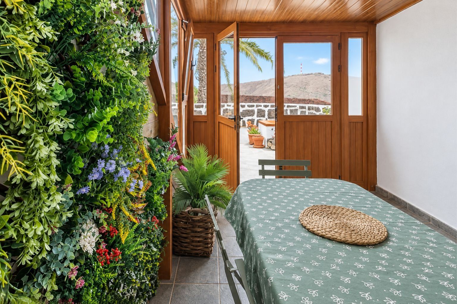 Una habitación con una cama, un banco, una planta en la pared y vistas a una colina.