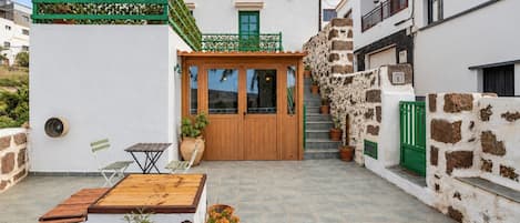A courtyard with a wooden door, potted plants, a small table, and a chair.