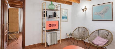 A room with a wooden ceiling, a radiator, a shelf with a 'GUEST READY' sign, two wicker chairs, and a framed map on the wall.